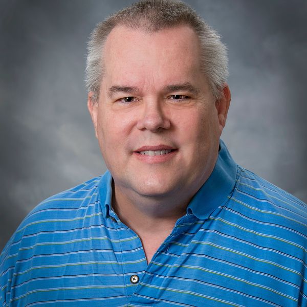 Middle-aged man smiling in a blue striped polo shirt.