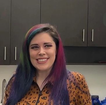 Smiling woman with colorful hair in a leopard print top.