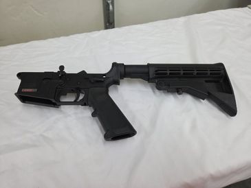 Black rifle lower receiver with adjustable stock on a white surface.