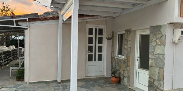 A stone-paved porch with white doors and a potted plant under a roof.
