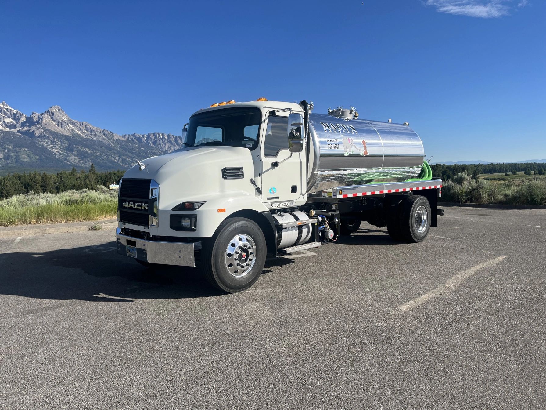 White Mack tanker truck parked with mountain backdrop on a clear day.
