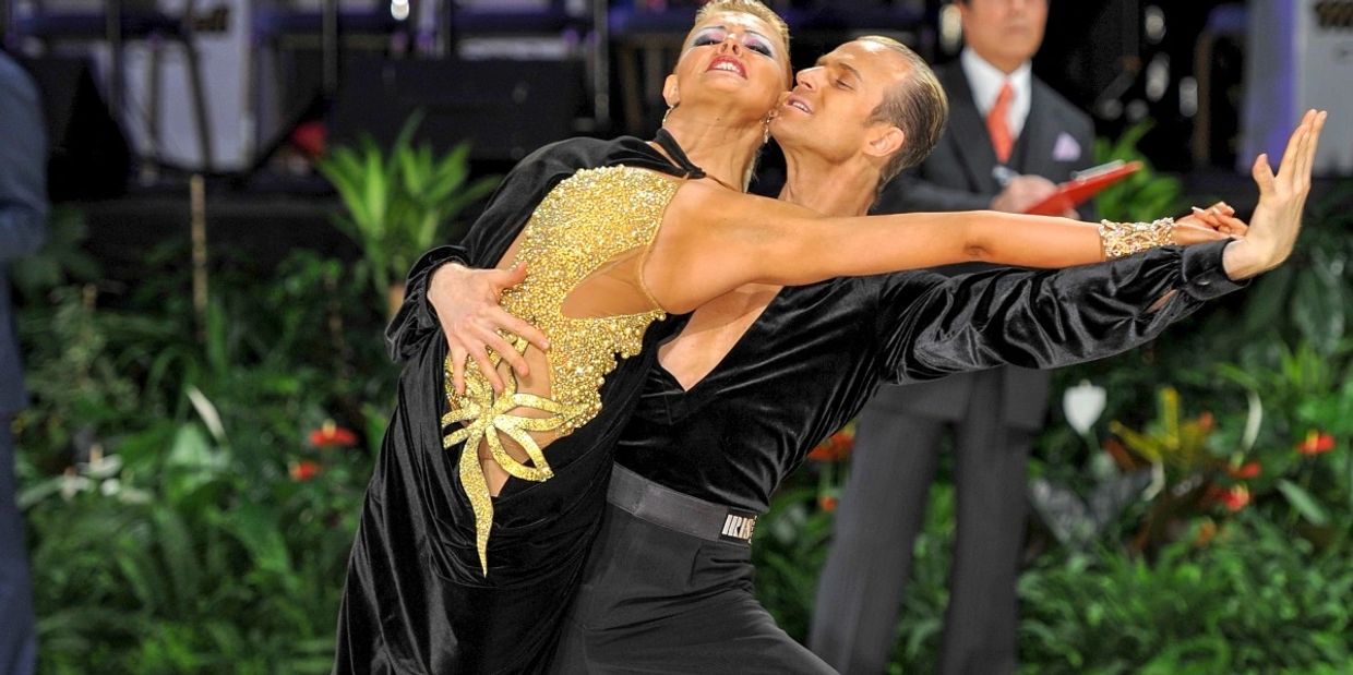 Elegant dance couple in black and gold costumes performing a dramatic ballroom pose.