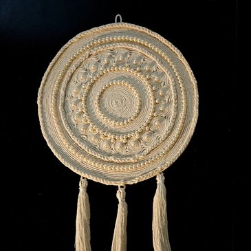 Circular woven wall hanging with tassels on a black background.