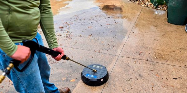 Man pressure washing a driveway near cactus plants.