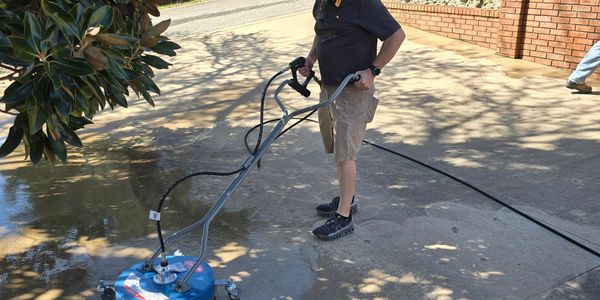 Man pressure washing a concrete driveway with a surface cleaner.