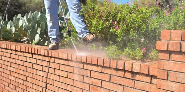 Person power washing a brick wall on a sunny day.