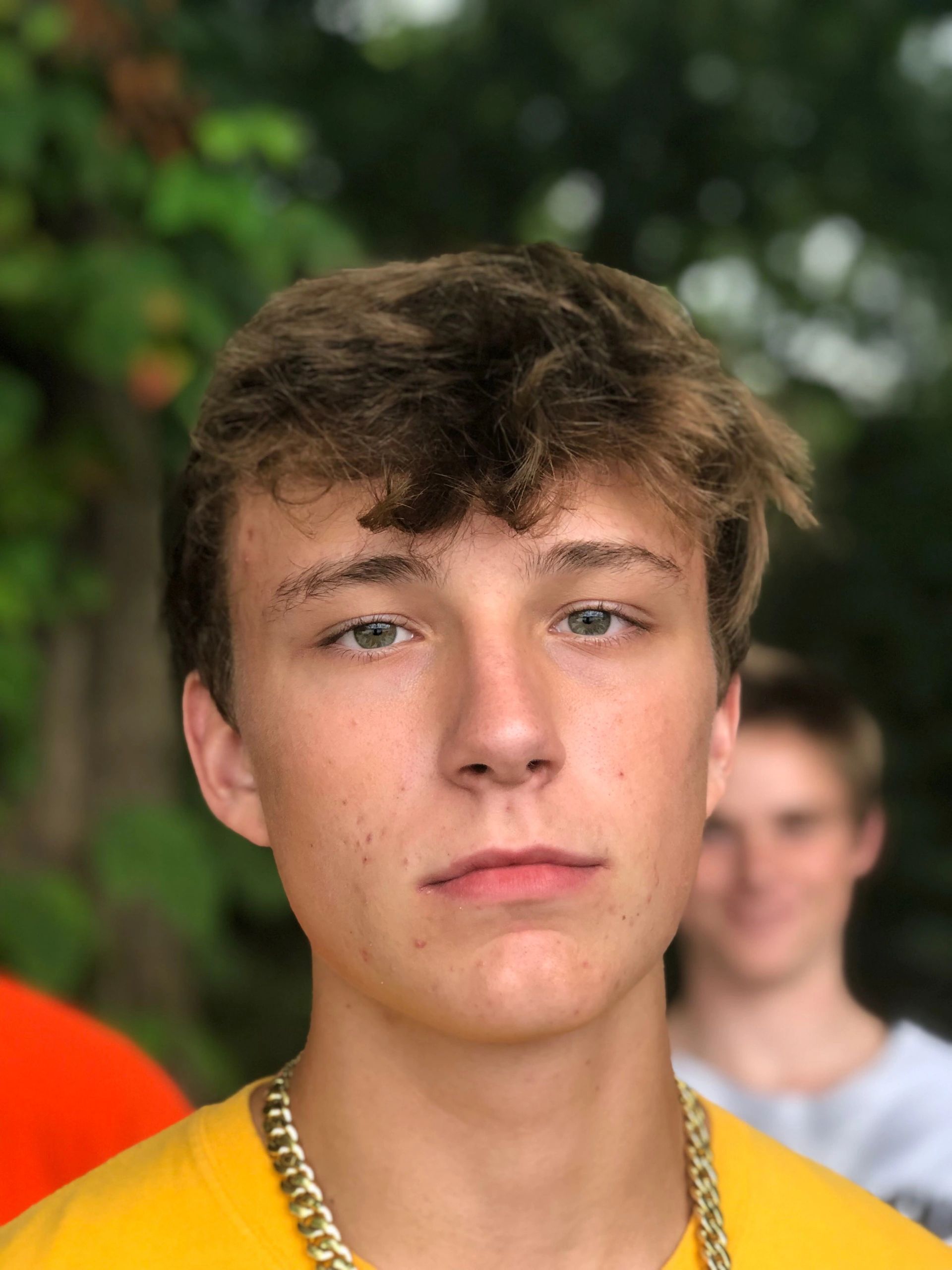 Close-up of a young man with green eyes and a gold chain.