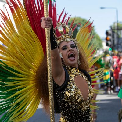 Performer in vibrant carnival costume with colorful feathers and crown.