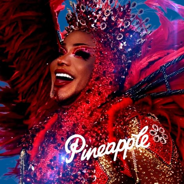 A vibrant performer in an elaborate red costume and crown, smiling joyfully.