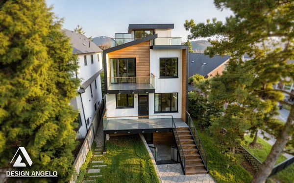 Modern three-story house with wood and white exterior surrounded by trees.