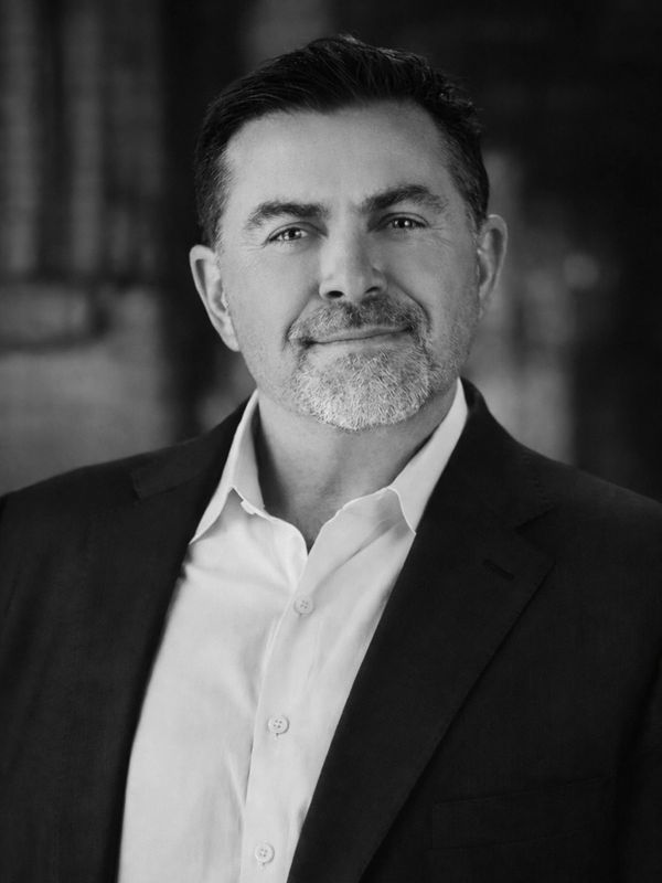 Confident middle-aged man in a suit smiling gently in a black and white portrait.