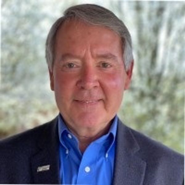 Smiling middle-aged man in a blue shirt and dark blazer, outdoors.