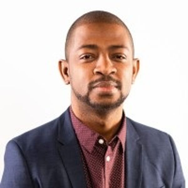 Confident man in a blazer and patterned shirt against a white background.