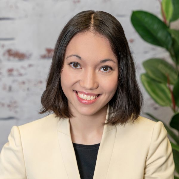Smiling woman in cream blazer with short dark hair, posing indoors.