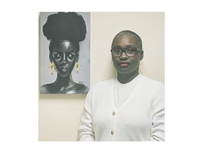 A woman in white stands beside a black and white portrait of a woman with large golden earrings.