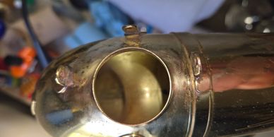Close-up of a shiny metal saxophone neck with an open hole.
