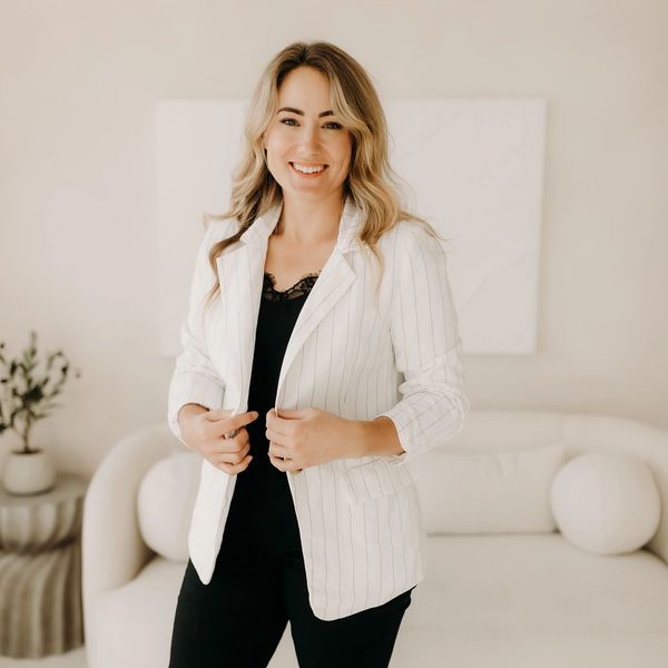 Smiling woman in white blazer standing indoors.