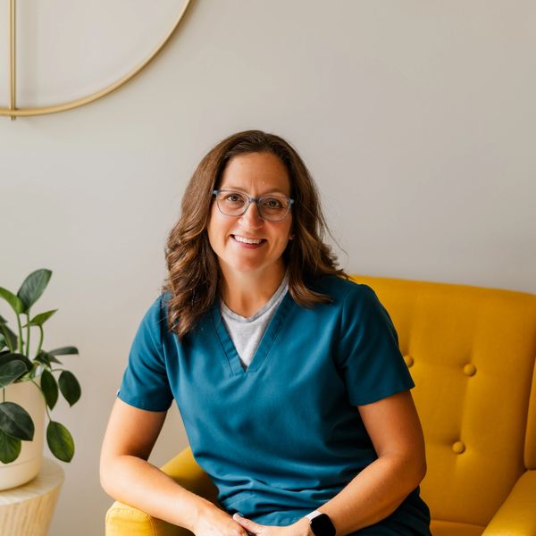 Smiling woman in teal scrubs sitting on a yellow chair.