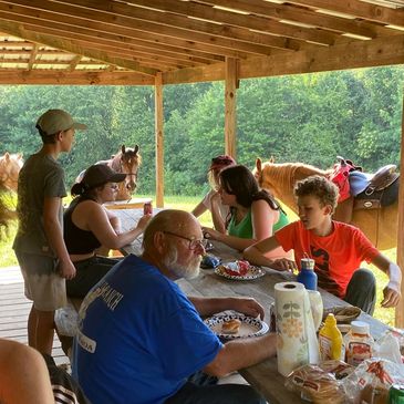 People enjoying a meal outdoors with horses nearby.