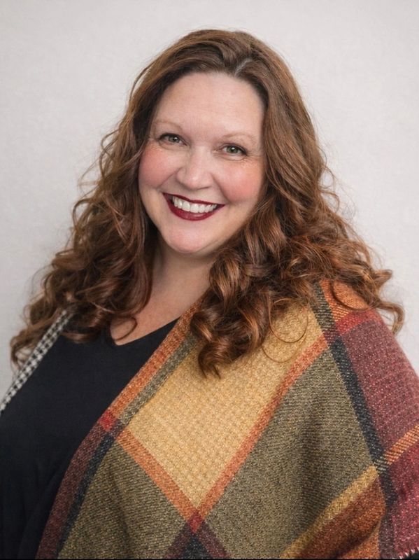 Smiling woman with curly hair wearing a colorful plaid shawl.
