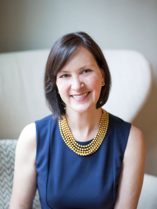 Smiling woman wearing a navy dress and a gold beaded necklace.