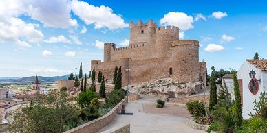 Historic castle atop a hill under a blue sky with scattered clouds.