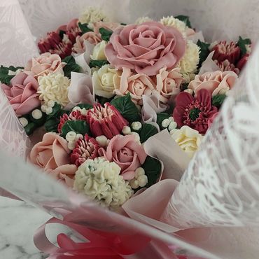 A bouquet of intricately crafted flowers in soft pink, cream, and red hues.