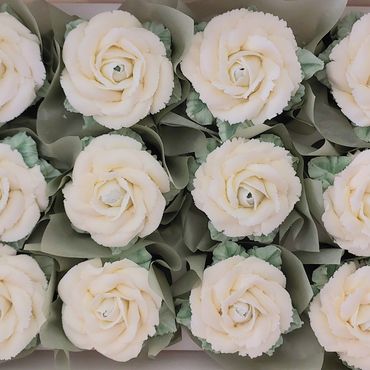 Twelve white rose-shaped cupcakes with green leaves in a box.