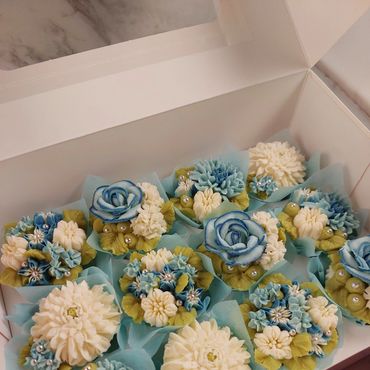 Cupcakes decorated with blue and white floral icing in a box.