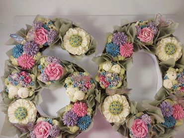Decorative floral arrangement shaped as the number 80 with pastel-colored flowers and butterflies.