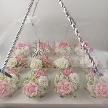 Elegant birthday cupcakes decorated with pink and white floral icing in a clear box.
