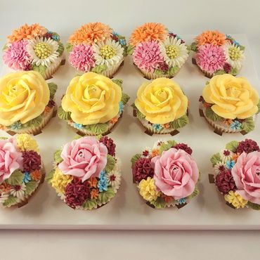 Twelve intricately decorated floral cupcakes arranged in three rows on a white tray.