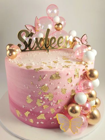 Elegant pink and gold sixteenth birthday cake with butterfly and pearl decorations.