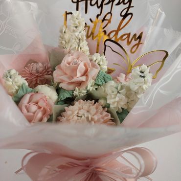 Delicate pastel flower bouquet with a golden "Happy Birthday" sign and butterfly decoration.