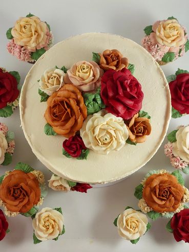 A cake and cupcakes decorated with realistic buttercream roses in red, orange, and cream colors.