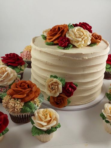 Elegant cream cake and cupcakes decorated with intricate buttercream flowers in autumn colors.