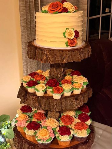 Rustic cake and cupcakes adorned with fall-colored rose decorations on wooden tiered stand.