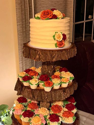 Three-tiered cake stand with white cake and rose-decorated cupcakes.