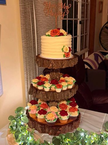 Rustic tiered cake and cupcakes with floral decorations on wooden stands.
