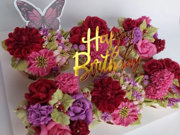 Colorful flower cupcakes with a golden Happy Birthday topper and a butterfly decoration.