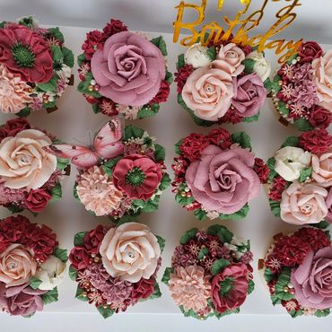 Cupcakes decorated with intricate pink and red flowers and a butterfly.