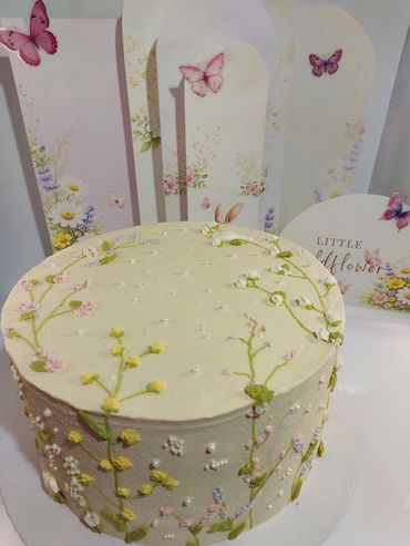 Elegant cake with delicate floral and butterfly decorations on a pastel backdrop.