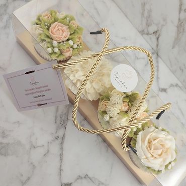 Elegant floral cupcakes in a clear box with a gold rope handle on marble.