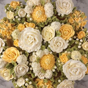 Cupcakes decorated with intricate yellow and white buttercream flowers on a marble surface.