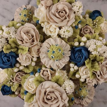 Intricately decorated cake with cream flowers in white, beige, blue, and green hues.