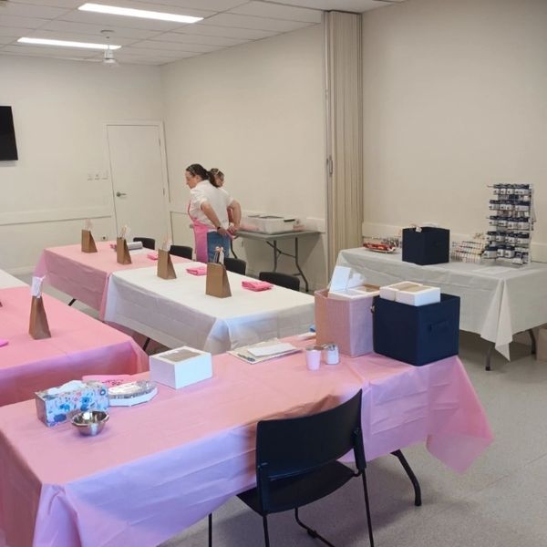 Room set up for a craft or workshop event with tables covered in pink and white cloths.