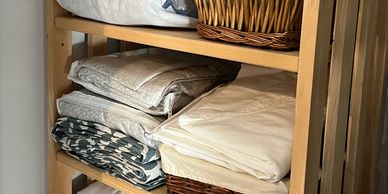 Wooden shelf holding neatly folded linens and wicker baskets.