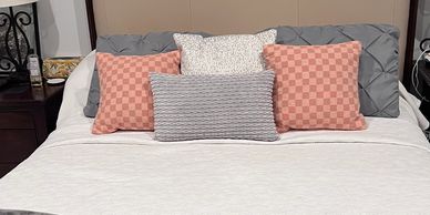 Neatly made bed with five decorative pillows in various patterns and colors.