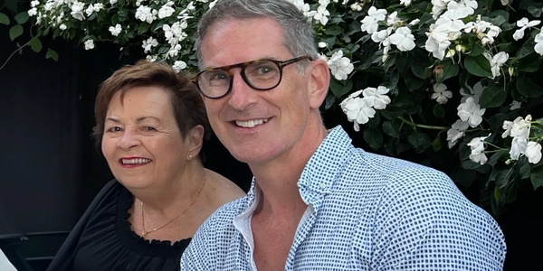 Two people smiling at a dining table with white flowers behind them.