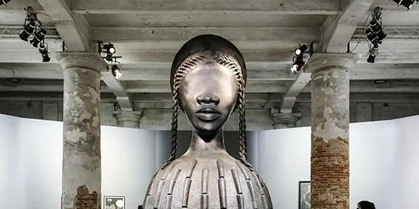 Abstract sculpture with braided hair in an industrial gallery.